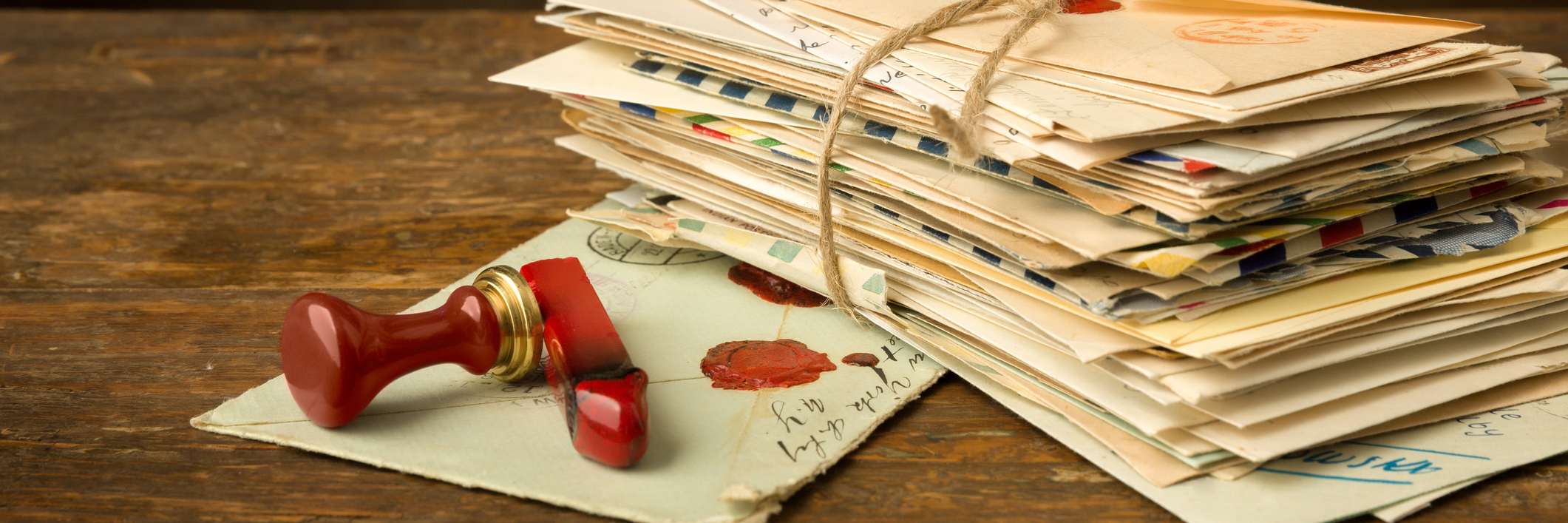 Stack of letters and a wax seal on a wooden surface.