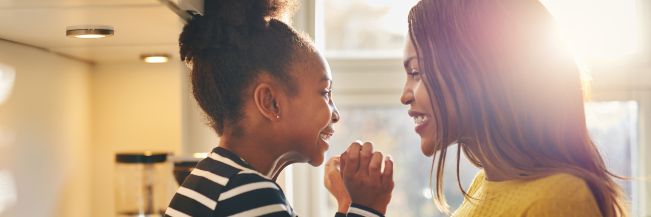 An African American woman and her young daughter smiling at each other.