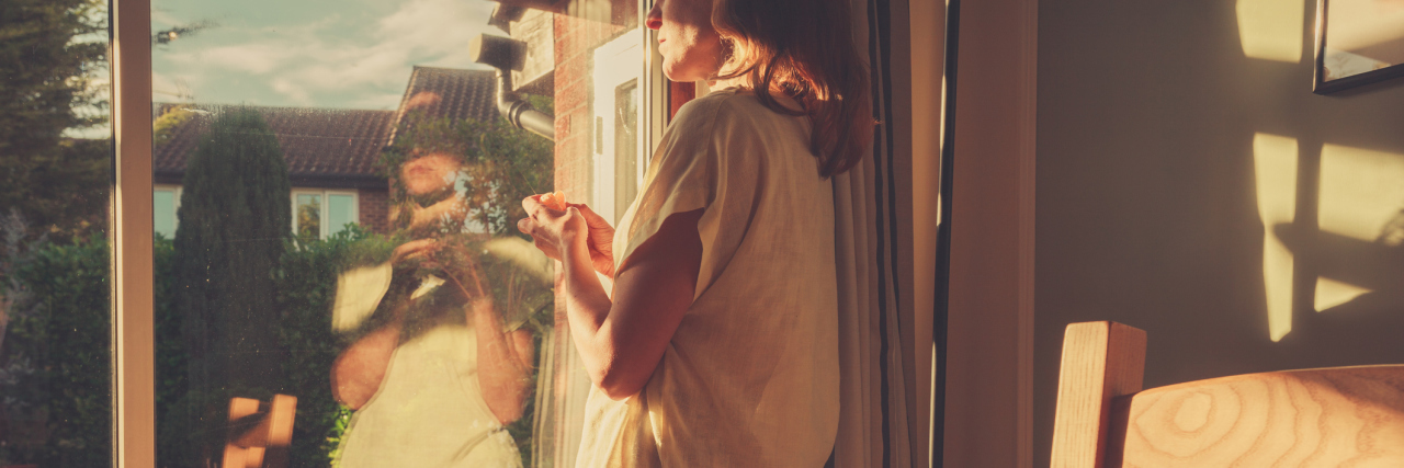 What I Realized About Recovery After Voluntary Psychiatric Admission young woman looking out of french doors at sunset