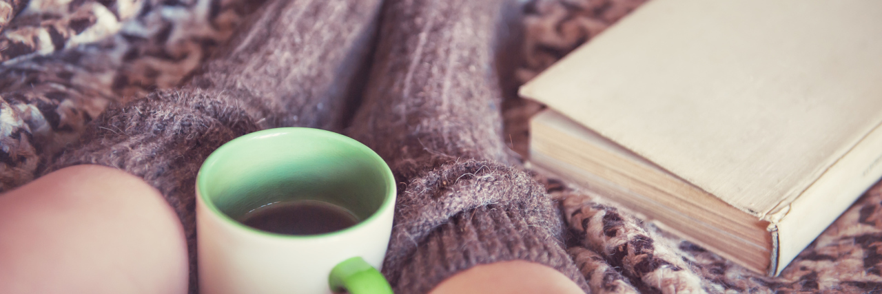 Adapting to New Lifestyle, Different Activities With Chronic Illness woman wearing thick socks in bed with a cup of tea and a book