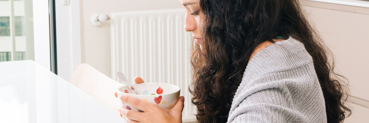 sad young woman with curly brown hair eating breakfast