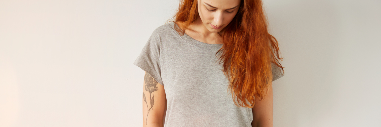 What Getting Tattoos Means to Someone With a History of Self-Harm Young girl wearing grey blank t-shirt and blue jeans. Concrete white wall background, flare light