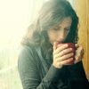 mid 30s woman standing in front of window with red cup of tea or coffee