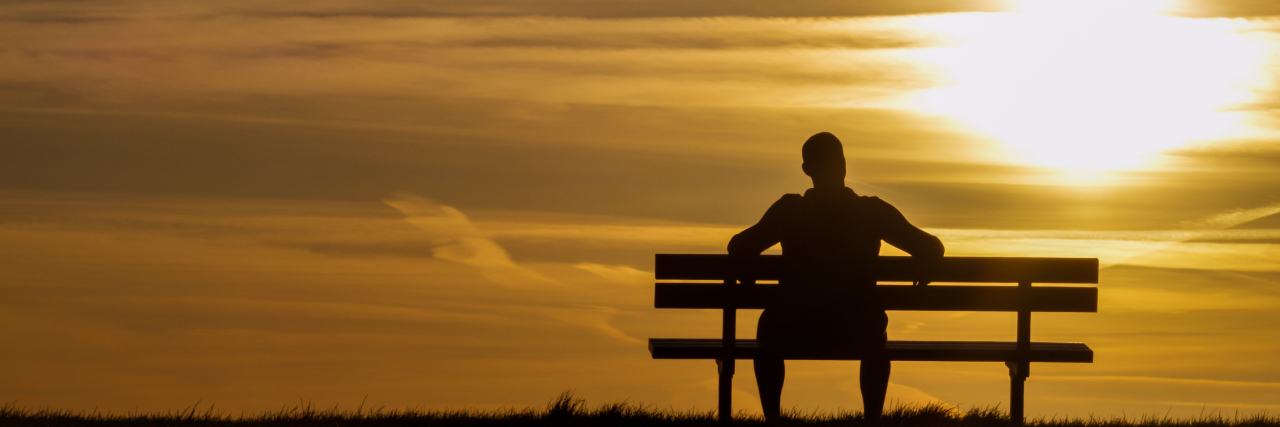 Silhouette man upon a bench looking towards sunset