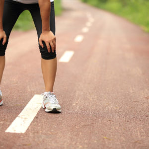 A tired female runner, taking a break from her run with her hands on her knees.