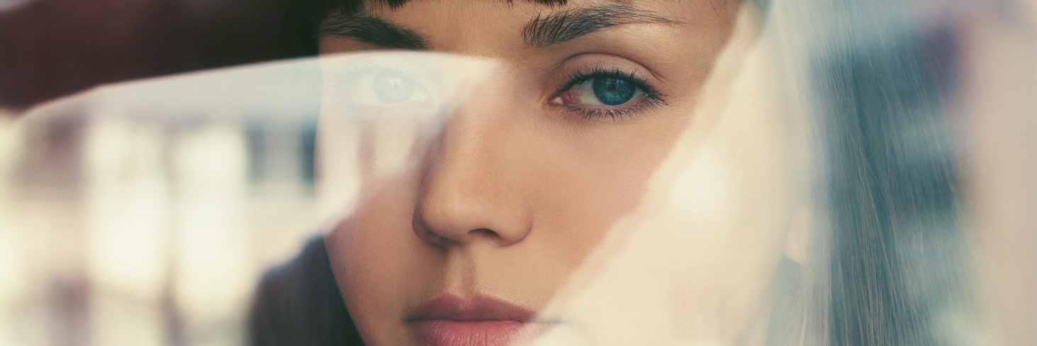 What It's Like to Experience Mixed Episodes With Bipolar Disorder woman looking through window at camera with window reflection overlaid