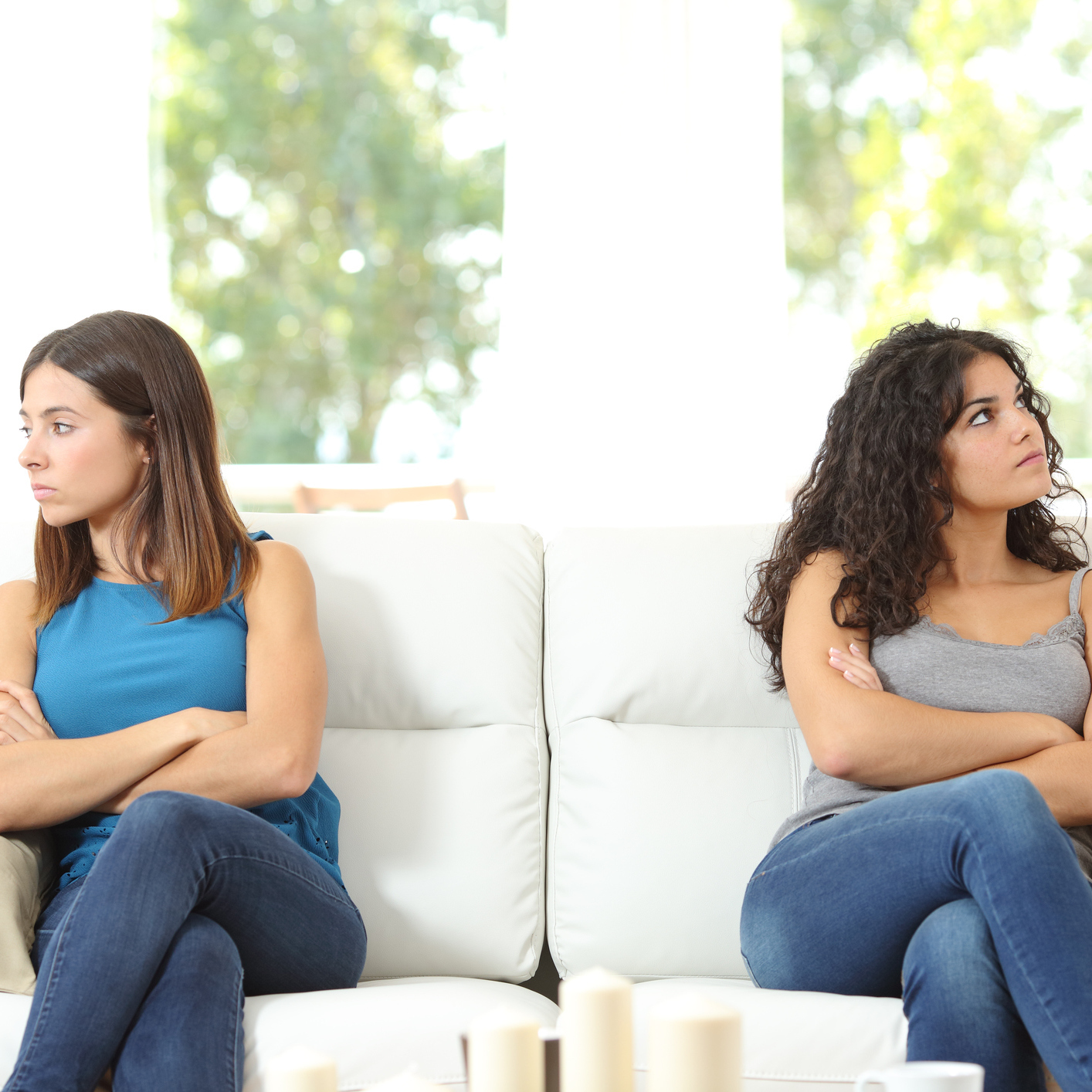 two friends sitting on opposite ends of the couch with arms crossed looking away from each other