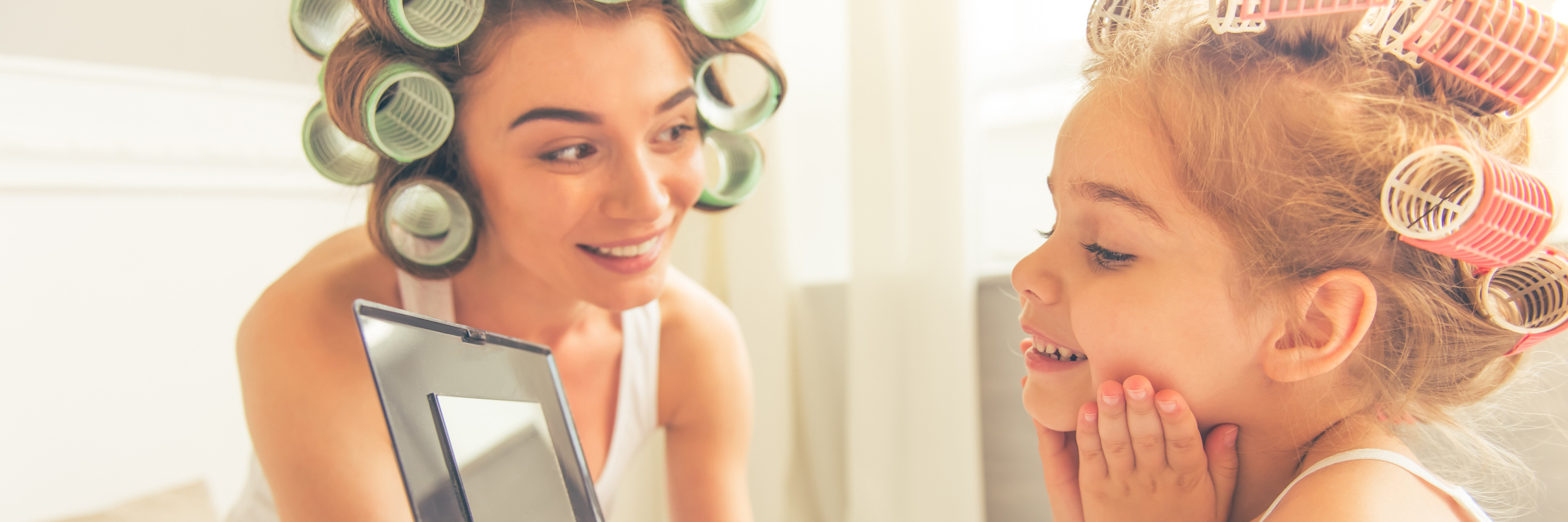 To the Chronically Ill Mom Who Can't Travel During Summer Vacation A mom and her young daughter, wearing curlers, looking into a mirror.