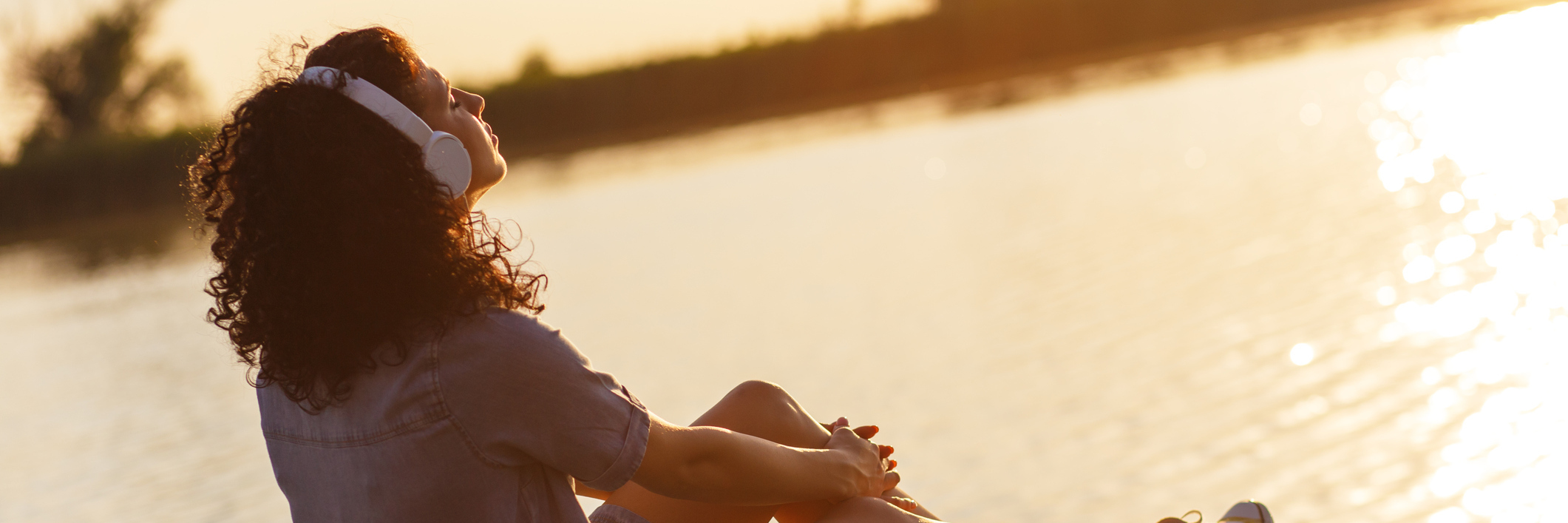 How to Lower Anxiety Every Day young woman listening to music or meditation on pier at sunset looking relaxed
