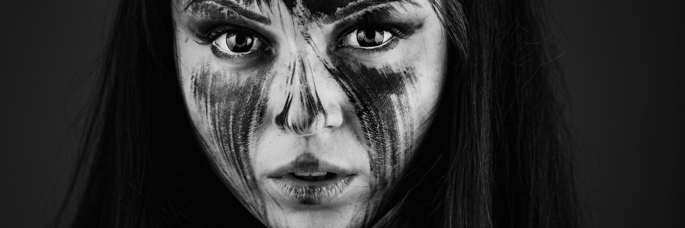 Please Don't Tell Me to 'Think Positive' About My Health A woman looking into camera, with black paint on some of her skin.