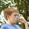A young boy using an inhaler outside.