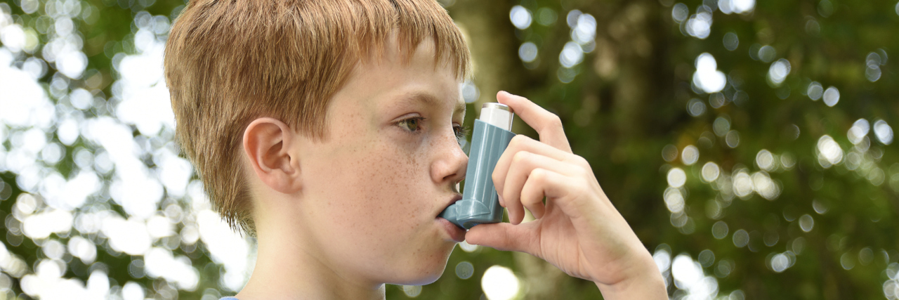 What You Should Know About Asthma, From an Asthma Mom A young boy using an inhaler outside.