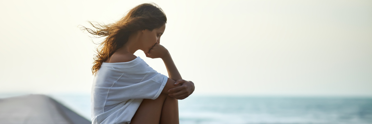 4 Ways I've Adapted to a Life With Chronic Illness A young woman sitting alone on a pier, looking at a body of water.