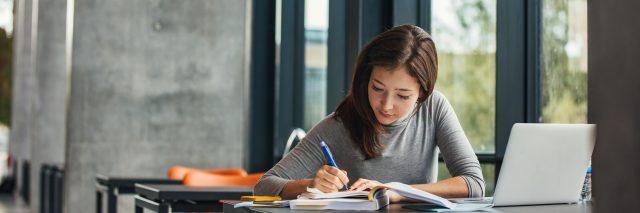 Shot of young asian female student sitting at table and writing on notebook. Young female student studying in library.