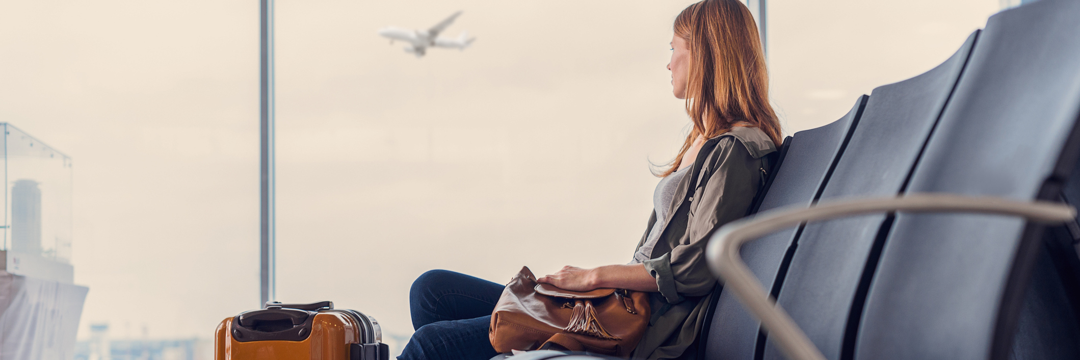 How to Deal With Anxiety and Still Enjoy Traveling woman waiting in airport with suitcase sitting in front of window