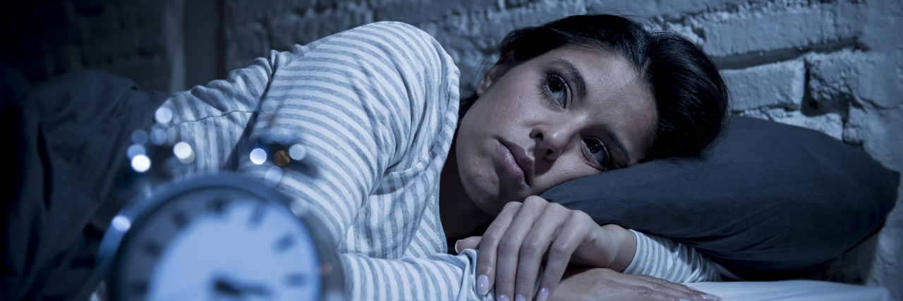 What It's Like to Have Sleepless Nights Because of Lupus A woman lying awake at night, with a clock in the foreground.