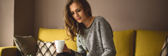 woman sitting at home on her couch drinking coffee
