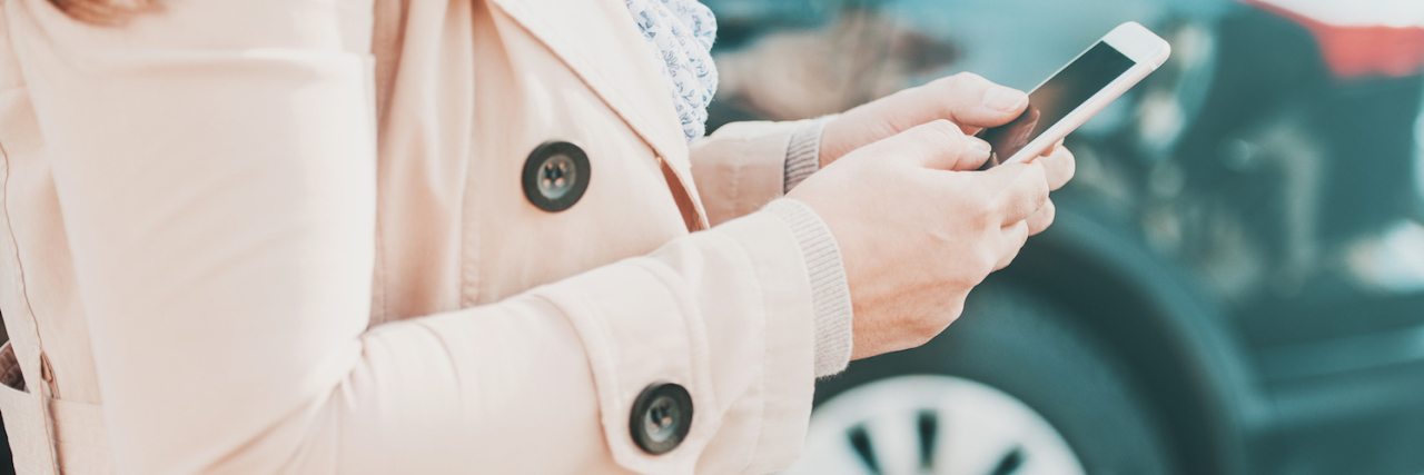 How a Geocaching Game Helps Me as Someone on the Autism Spectrum Woman holding phone, standing near car outdoors