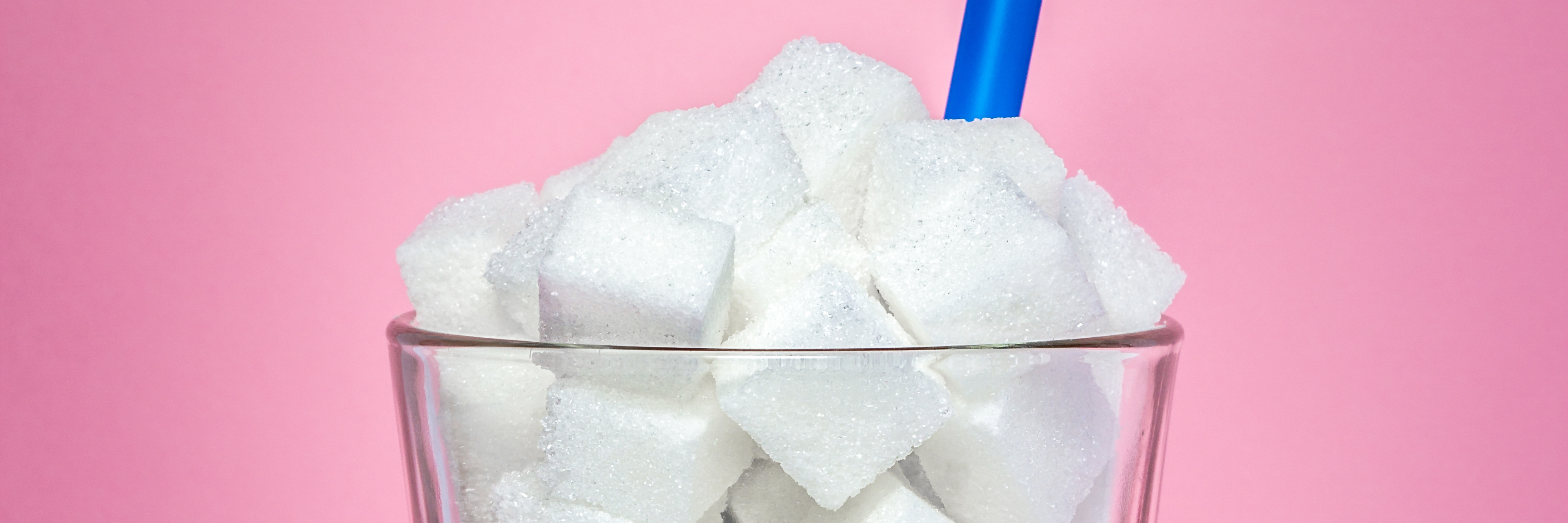Glass full of sugar cubes on a pink background with a blue straw