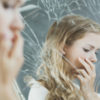 upset girl standing in front of broken mirror with focus on reflection