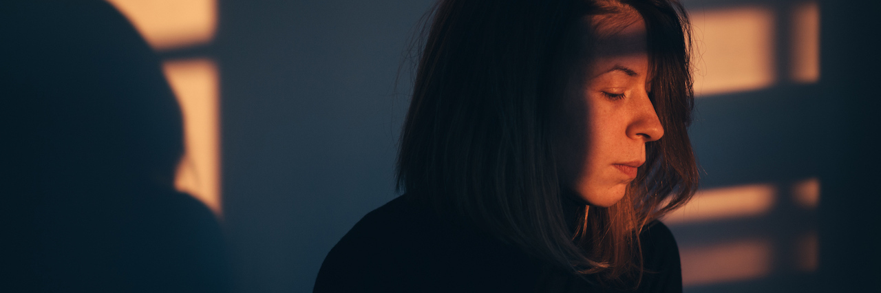 A woman sitting in darkness, with light coming through a window