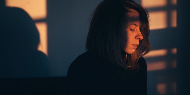 A woman sitting in darkness, with light coming through a window