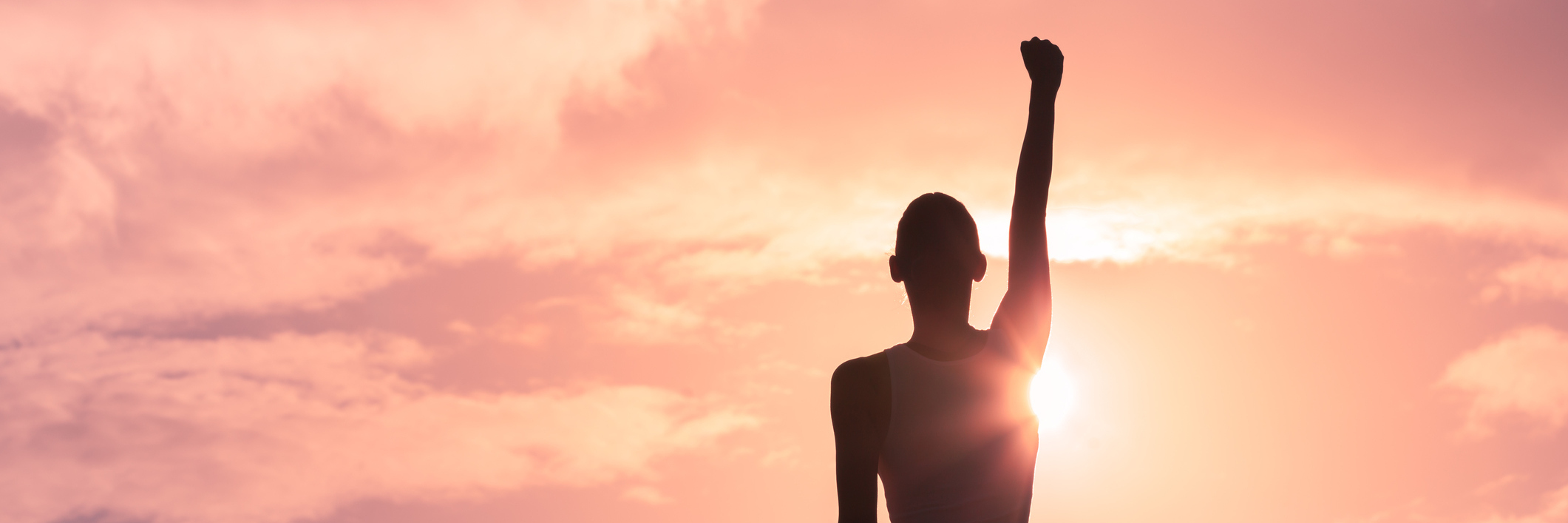 woman raising her arm in victory at sunset