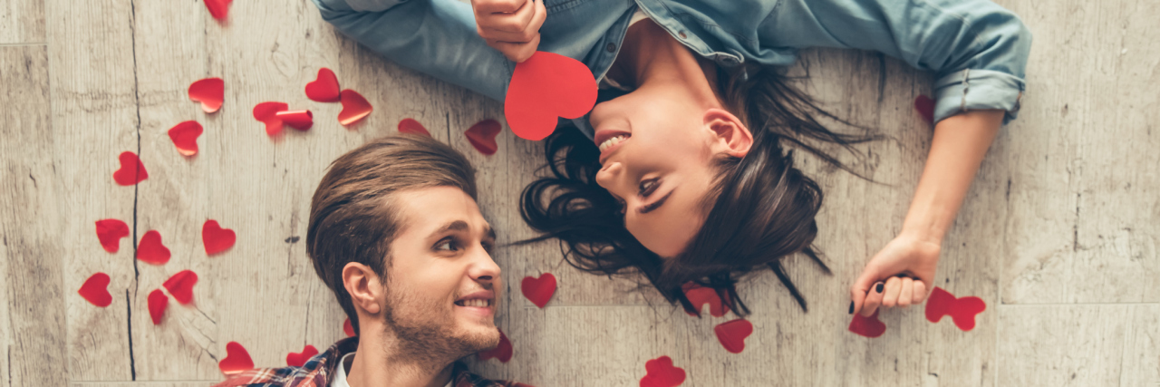 A young couple, laying on the floor, with paper hearts around them.
