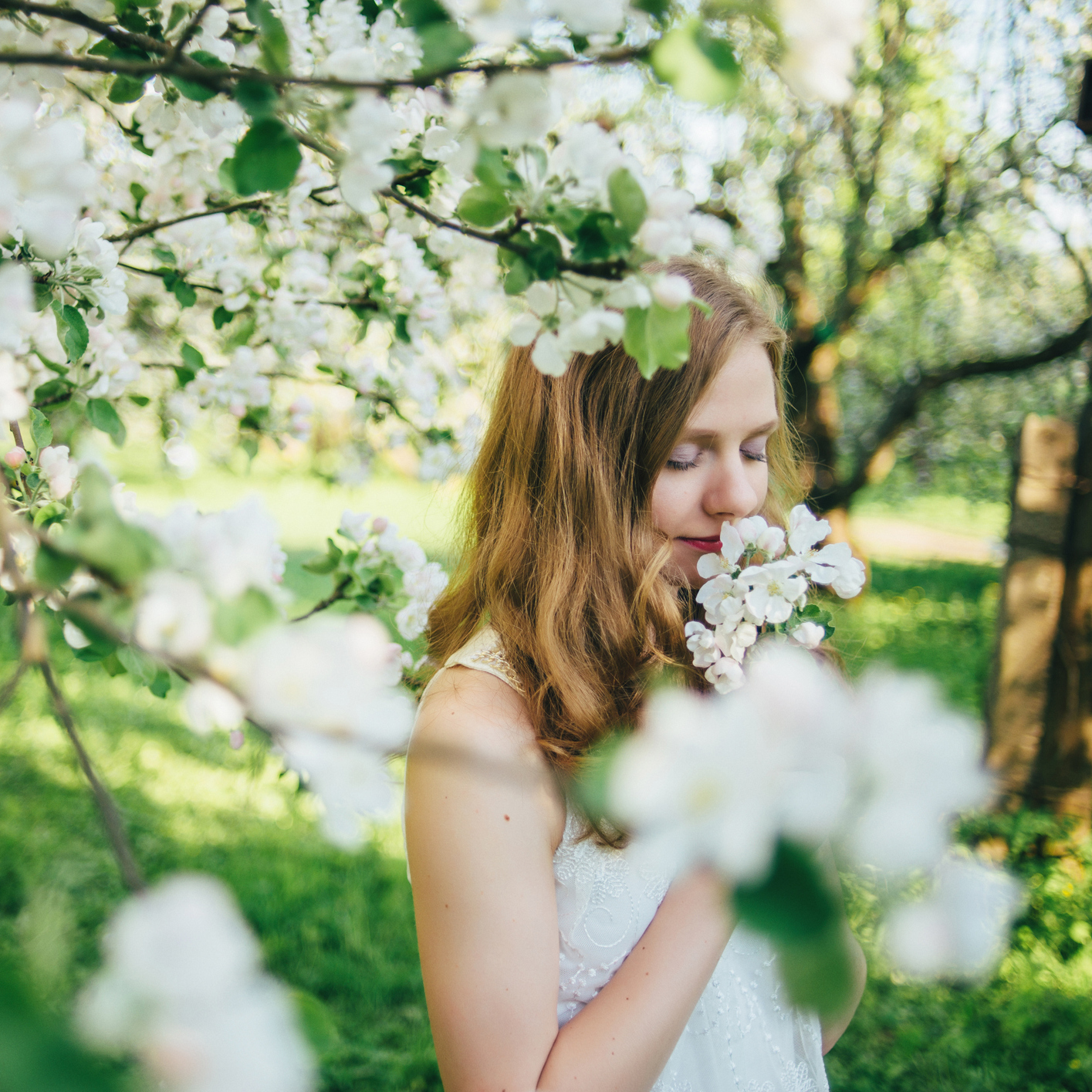 A girl in a white dress, in an apple orchard, smelling flowers.