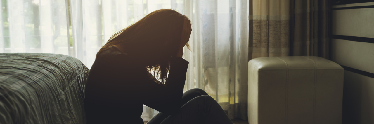Why We Need to Take Mental Health 'Sick Days' Seriously depressed woman sitting in the dark bedroom