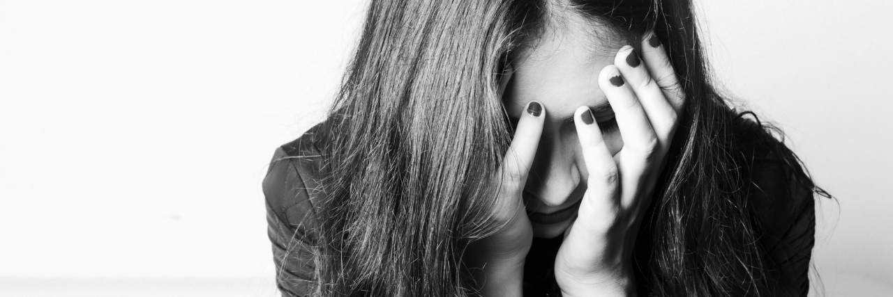 The 5 Stages of Grief I Experienced After Becoming Chronically Ill A sad woman holding her face in her hands.