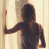sepia tone photo of girl holding curtain open in room with back turned to camera
