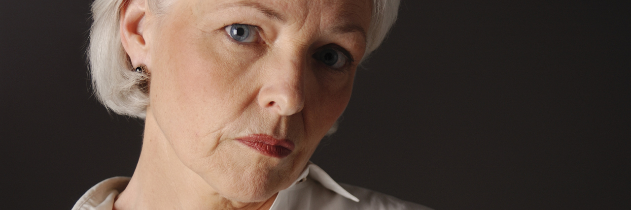 When I Realized I Was Putting Myself Down By Minimizing My Illness An older woman with a serious expression, looking into the camera.