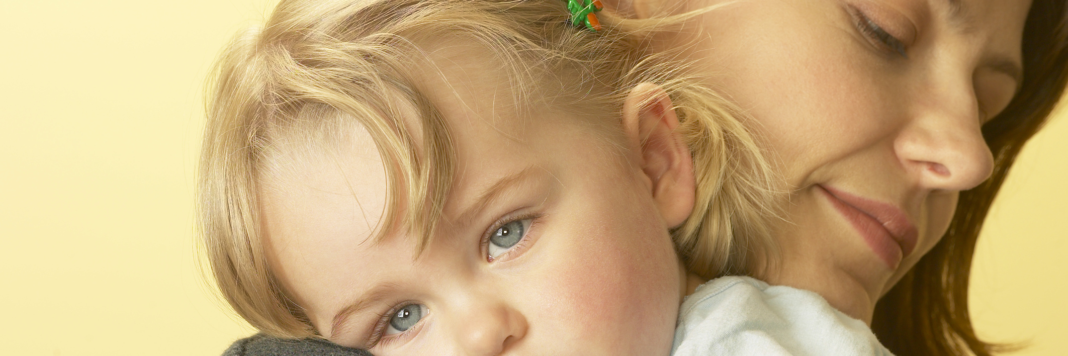 The Cost of Mental Health in Parenthood mother consoling sad daughter against yellow background