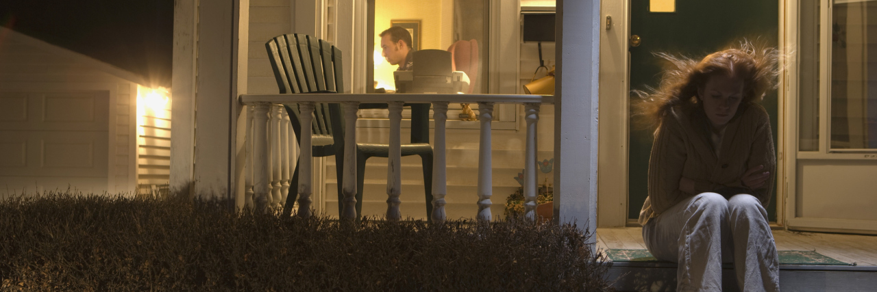 Why Communication Is Important for Spouses With Anxiety woman sitting outside house on steps looking upset while husband sits inside