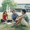 three students sitting outdoors on campus with their school work