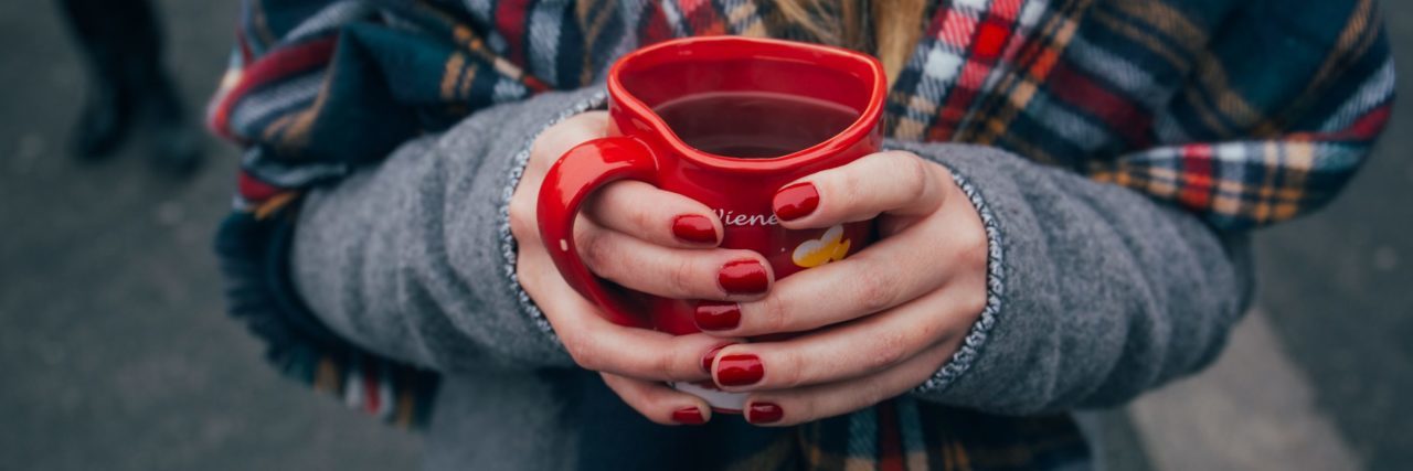 woman with blonde hair holding mug of hot drink wearing scarf outside