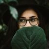 woman wearing glasses covering face with leaf