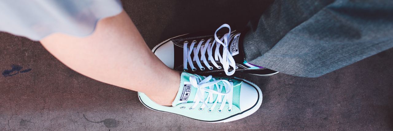 man and woman wearing converse sneakers in bright and dark color, feet facing opposite