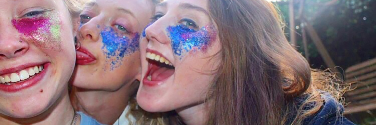 three young women smiling wearing colorful glitter around eyes