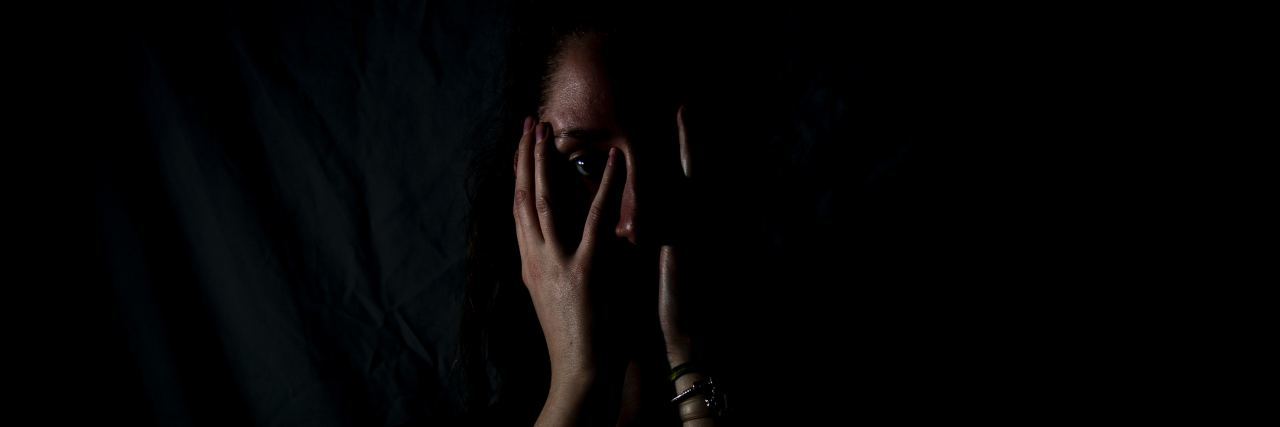 A woman stands in a dark room with her face covered