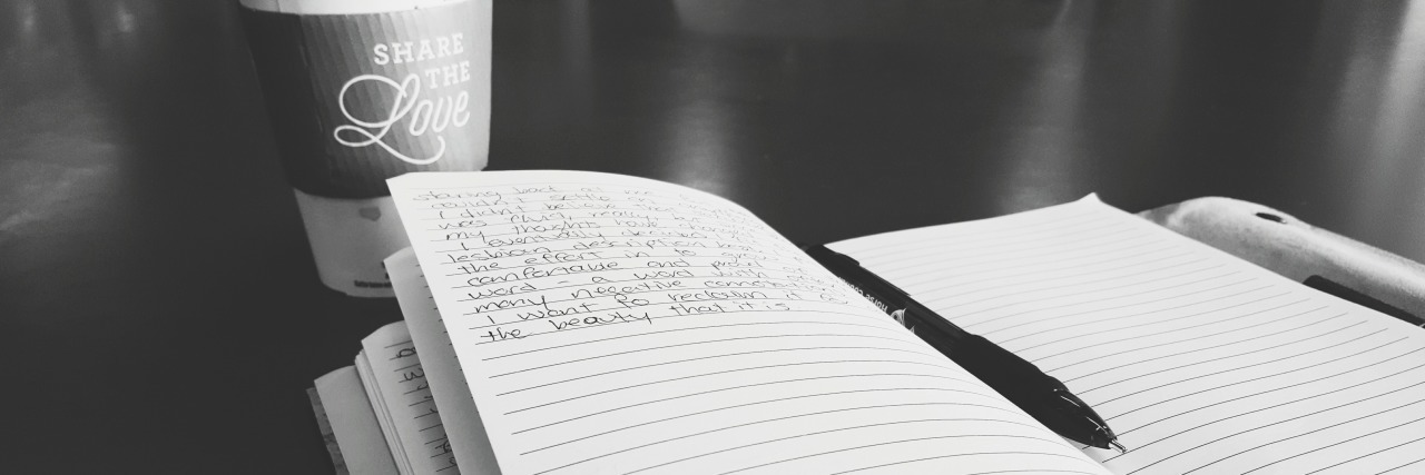 A journal and pen by a cup of coffee.