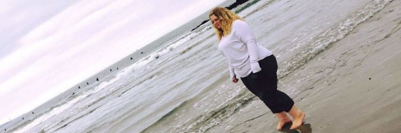 To the People Who Feel Sorry for My Life With Endometriosis The writer walking on the beach, with a hashtag that reads, "I'll rise up."