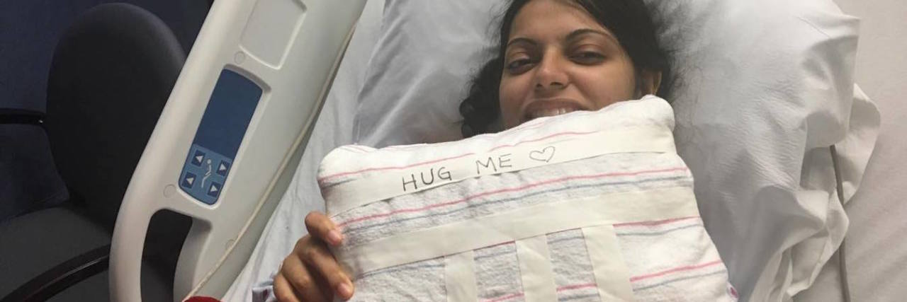Thoughts Before My First Open-Heart Surgery the author in a hospital bed, holding a pillow that says hug me
