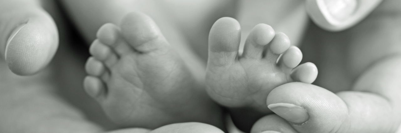 The NICU Made Me A Better Mom Mother gently hold baby legs in hand.