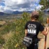 woman hiking in the mountains with a black shirt on that says 'this shirt turns black whenever I am in pain'