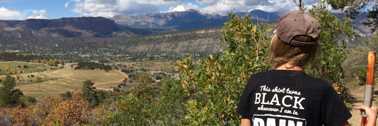 What to Think About During Discussions of Opioids and Chronic Pain woman hiking in the mountains with a black shirt on that says 'this shirt turns black whenever I am in pain'
