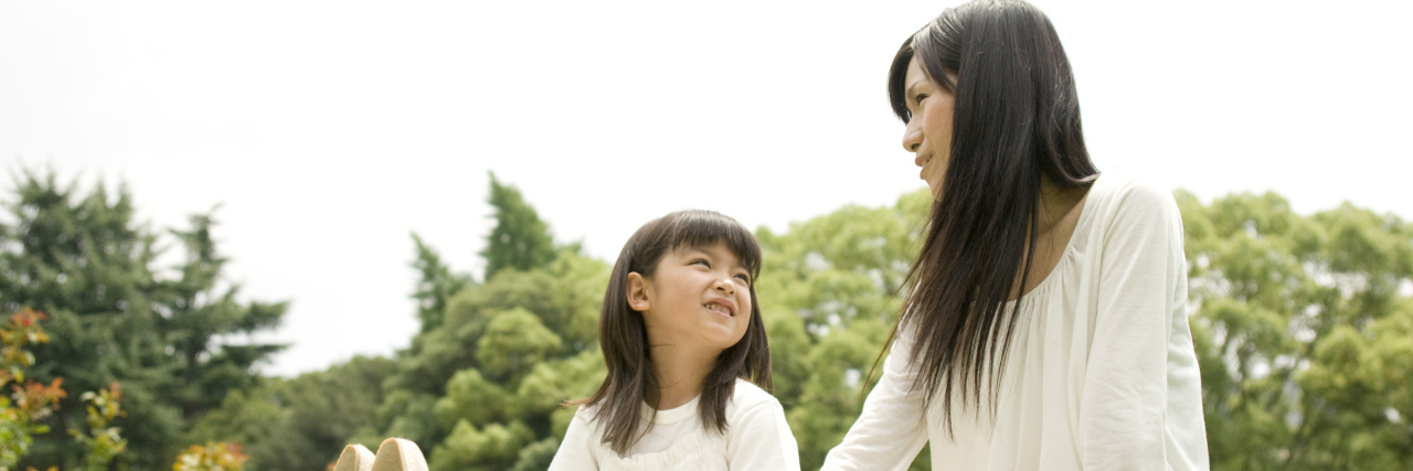How Parents Can Help Children Understand Disability Mother and daughter sitting outside together on a lawn.