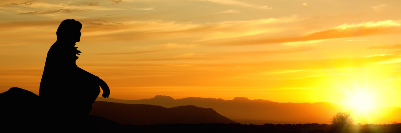 Silhouette of woman sitting on rock, watching sunset