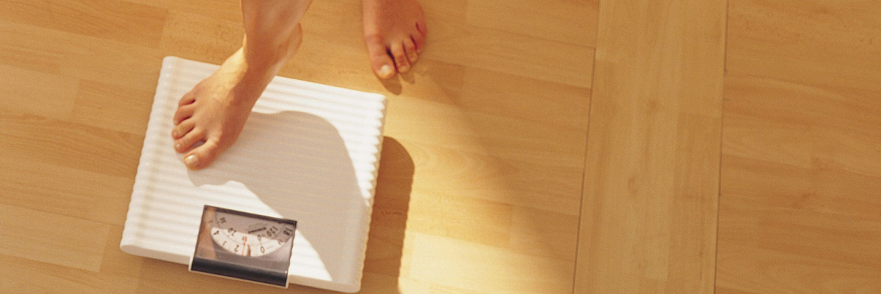 Why We Need to Talk About 'Scale Trauma' in Eating Disorder Recovery woman stepping onto scale